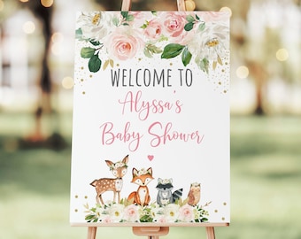 May include: A white welcome sign with pink and white flowers, gold glitter, and a pink heart. The sign says "Welcome to Alyssa's Baby Shower" with a deer, fox, raccoon, and owl illustration.