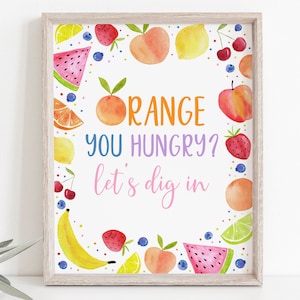 May include: A printable sign with a white background and a colorful border of fruit illustrations. The text on the sign reads "Orange you hungry? Let's dig in".