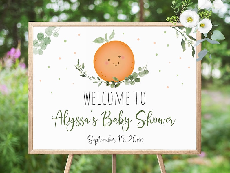 May include: A white welcome sign with a green leafy border and a smiling orange illustration. The text reads "Welcome to Alyssa's Baby Shower September 15, 20xx".