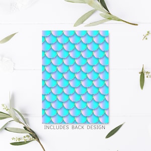 K&ouml;nnte beinhalten: Ein blaues und violettes Meerjungfrauen-Schuppenmuster mit goldenen Glitzerakzenten. Das Muster wiederholt sich auf wei&szlig;em Hintergrund. Der Text "INCLUDES BACK DESIGN" ist unter dem Muster gedruckt.
