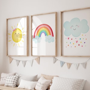 May include: Three framed prints with a cartoon sun, rainbow, and cloud with raindrops. The sun has a pink bow and a smiling face. The rainbow has a smiling cloud above it. The cloud has a smiling face and is raining hearts and stars.
