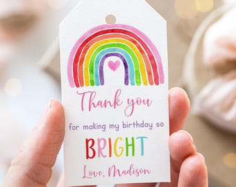 May include: Rainbow-themed thank you tag with the text "Thank you for making my birthday so BRIGHT Love, Madison". The rainbow is painted in watercolor style with a pink heart in the center.