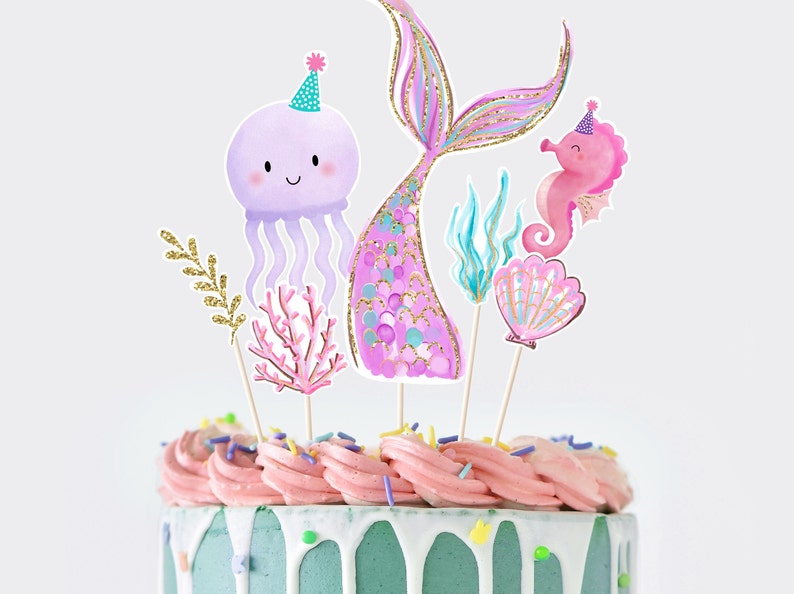 May include: A cake decorated with pink and purple frosting and topped with mermaid-themed cake toppers, including a mermaid tail, a jellyfish, a seahorse, and a seashell.