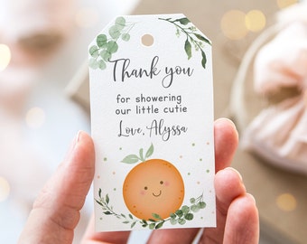 May include: Thank you for showering our little cutie. Love, Alyssa. A white baby shower favor tag with green leaves and a smiling orange illustration.