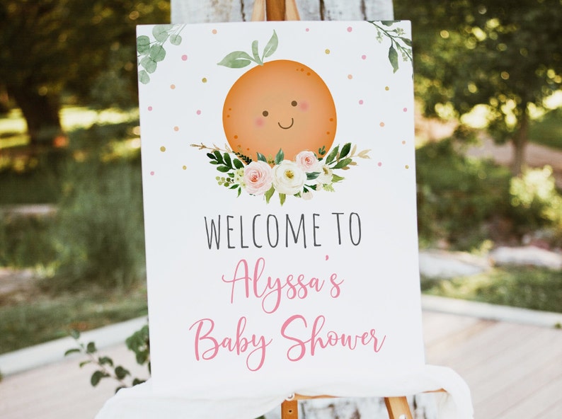 May include: A white welcome sign with a cute orange illustration and pink floral accents. The text reads "Welcome to Alyssa's Baby Shower".
