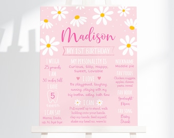 May include: Pink and white first birthday sign with daisies and the name Madison. The sign lists the child's weight, height, number of teeth, favorite foods, books, and songs.