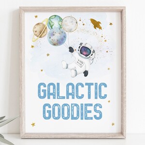 May include: A printable sign with a blue background and white text that says "Galactic Goodies". The sign features a cartoon astronaut holding balloons shaped like planets and stars.