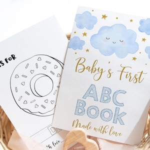 May include: Two baby books in a woven basket. One book has a donut illustration with the text "D is for". The other book is titled "Baby's First ABC Book" with blue clouds and stars, and the text "Made with love".