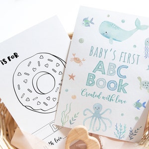 Può includere: Un libro illustrato per bambini con un tema oceanico ad acquerello. La copertina presenta una balena, un polpo, un granchio, una tartaruga e un pesce. Il testo recita "Baby's First ABC Book Created with Love".