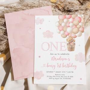 May include: Pink and white first birthday invitation with a teddy bear in a hot air balloon. The invitation says "Join us to celebrate Madison's beary 1st birthday" and includes the date, time, and location of the party.