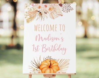 May include: Welcome to Madison's 1st Birthday sign with a white background, pink text, and a watercolor illustration of a pumpkin, flowers, and dried palm leaves.