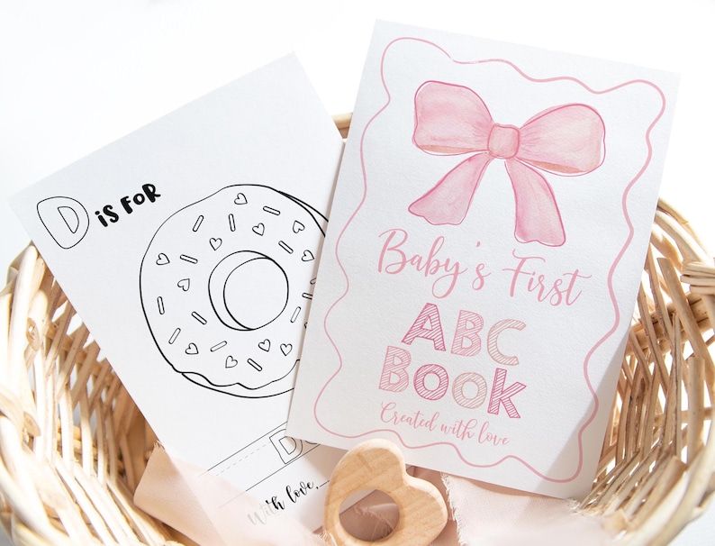 May include: A pink and white baby's first ABC book with a pink bow on the cover. The text on the cover reads "Baby's First ABC Book Created with love".