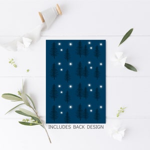 May include: A navy blue card with a repeating pattern of stylized evergreen trees and white stars. The text "INCLUDES BACK DESIGN" is at the bottom. The card is on a white wooden surface with decorative elements.