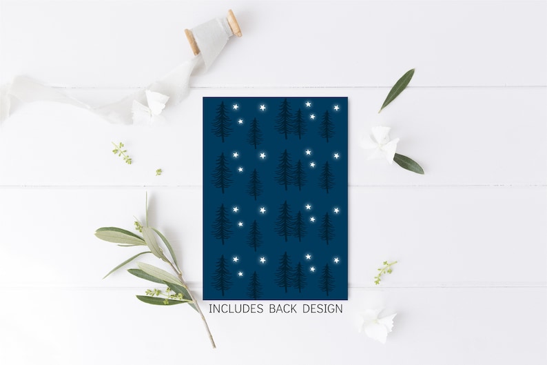 May include: A navy blue card with a repeating pattern of stylized evergreen trees and white stars. The text "INCLUDES BACK DESIGN" is at the bottom. The card is on a white wooden surface with decorative elements.