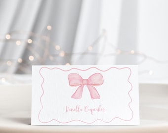 May include: A white card with a pink bow and the text "Vanilla Cupcakes" in pink script.