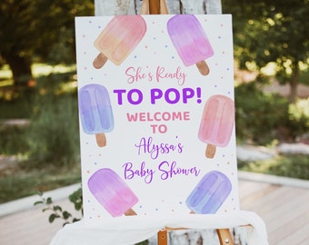 May include: A white baby shower sign with the text "She's Ready To Pop! Welcome to Alyssa's Baby Shower". The sign is decorated with colourful popsicle illustrations.