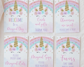 May include: Six pastel-colored party signs with unicorn illustrations and gold glitter accents. Each sign has a different message, including "Welcome to a Magical Day" and "Favors Take Some Magic Home."
