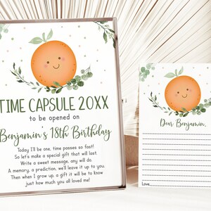 Puede incluir: Un letrero de c&aacute;psula del tiempo enmarcado y una tarjeta a juego. El letrero dice "TIME CAPSULE 20XX para abrir en el 18 cumplea&ntilde;os de Benjamin" con una ilustraci&oacute;n de naranja sonriente y vegetaci&oacute;n. La tarjeta dice "Querido Benjamin" con l&iacute;neas para escribir.