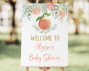 Puede incluir: Un cartel de bienvenida blanco con una ilustración de melocotón y detalles de purpurina dorada. El texto dice "Bienvenido al Baby Shower de Alyssa".