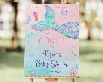 May include: A mermaid-themed baby shower welcome sign on an easel. The sign features a mermaid tail, seahorse, and jellyfish illustrations. Text reads "Welcome to Alyssa's Baby Shower" and the date. The background is a gradient of pink and teal.