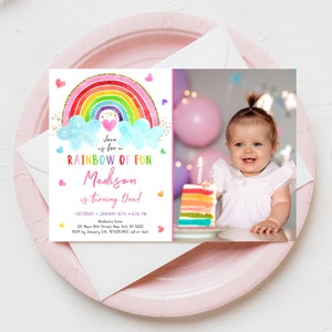 May include: A rainbow-themed first birthday party invitation with a photo of a baby girl. The invitation features a rainbow with clouds, hearts, and glitter. The text reads "Join us for a Rainbow of Fun Madison is turning One!" with the date, time, and location of the party.