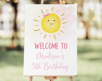 May include: Welcome to Madison's 5th Birthday sign with a pink and gold watercolor background and a cartoon sun with a pink bow.