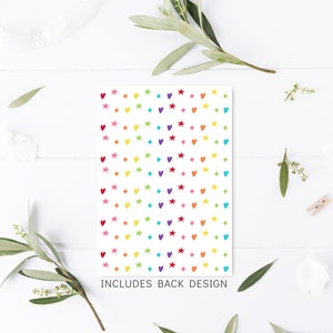 Peut inclure: Une carte blanche avec un motif color&eacute; de c&oelig;urs et d'&eacute;toiles. Le texte "INCLUDES BACK DESIGN" est imprim&eacute; en bas de la carte.