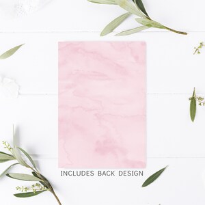 Puede incluir: Una tarjeta rosa en blanco con textura de m&aacute;rmol. La tarjeta est&aacute; sobre una superficie de madera blanca con ramitas verdes y flores blancas.