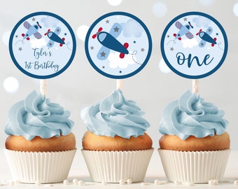 May include: Three blue and white cupcake toppers with a blue airplane design. The toppers say "Tyler's 1st Birthday" and "one".