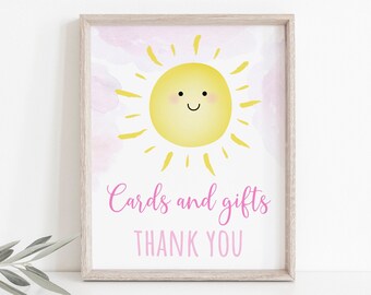 May include: A printable sign with a yellow sun with a smiling face on a pink watercolor background. The text "Cards and gifts Thank You" is written in pink below the sun.