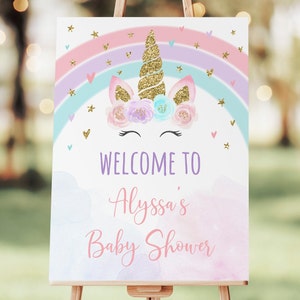 May include: A welcome sign for a baby shower with a unicorn illustration. The unicorn has a gold horn and a floral crown. The sign has a rainbow and clouds with the text "Welcome to Alyssa's Baby Shower".