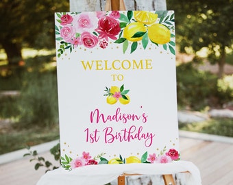 May include: Welcome to Madison's 1st Birthday sign with a watercolor floral design featuring pink and red roses, green leaves, and yellow lemons. The background is white with gold glitter.
