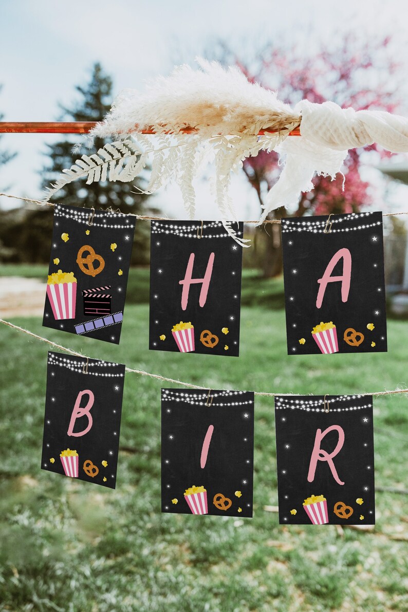 May include: A black and white banner with pink letters spelling "HABIBIR" with a popcorn and pretzel design on each flag. The banner is strung with white string and is hanging from a metal rod.