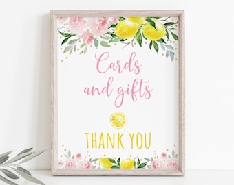 May include: A white sign with a pink floral border and gold glitter accents. The sign says "Cards and gifts" with a lemon slice graphic and "Thank you" in gold lettering.