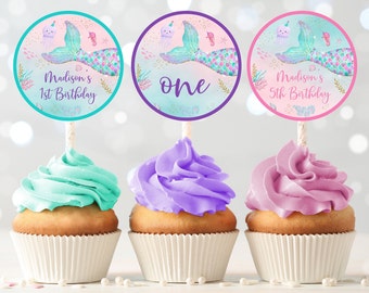 May include: Three mermaid-themed cupcake toppers with a pink, purple, and turquoise background. The toppers feature a mermaid tail, a seahorse, and a jellyfish. The text on the toppers reads "Madison's 1st Birthday", "One", and "Madison's 5th Birthday".