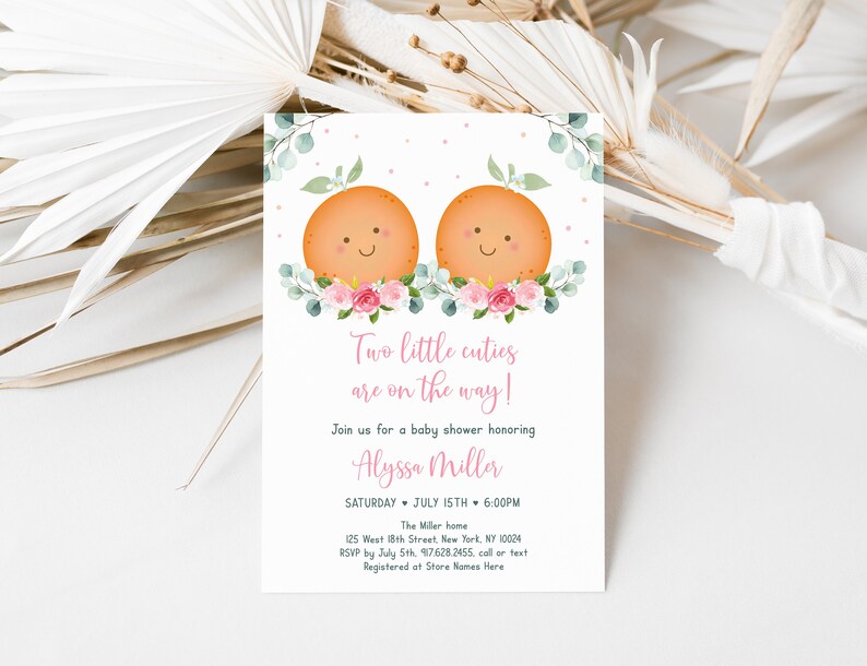 Puede incluir: Una invitaci&oacute;n a un baby shower con un dise&ntilde;o floral rosa y verde. Dos ilustraciones de frutas naranjas con caras sonrientes est&aacute;n en la parte superior de la invitaci&oacute;n. El texto dice "&iexcl;Dos peque&ntilde;os encantos est&aacute;n en camino!" y "&Uacute;nete a nosotros para un baby shower en honor a Alyssa Miller".