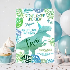 May include: A green and blue dinosaur silhouette with a party hat on its head. The dinosaur is surrounded by green and blue tropical leaves. The text "STOMP, CHOMP AND CHEW" is at the top of the invitation. The text "OUR LITTLE DINO MATTHEW IS TWO" is below the dinosaur. The invitation also includes the date, time, and location of the party.