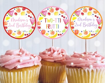May include: Three cupcakes with pink frosting and white sprinkles. Each cupcake has a circular topper with a fruit design and text. The toppers read "Madison's 2nd Birthday" and "TWO-TTI FRUTTI". The toppers have red, pink, and orange borders.