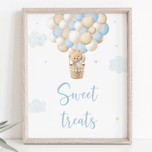 May include: A framed print with a watercolor illustration of a teddy bear in a hot air balloon made of blue and beige balloons. The text "Sweet treats" is written below the balloon.