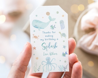 Op de afbeelding: Een wit label met een aquarelontwerp met een walvis, vissen, krab, kwal en schildpad. Op het label staat "Bedankt om van mijn verjaardag een Splash te maken, Love, Oliver."