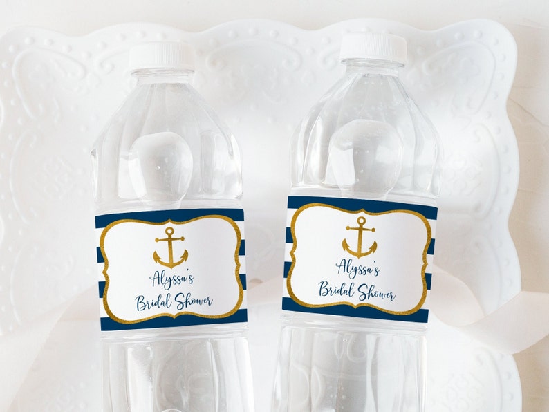 K&ouml;nnte beinhalten: Zwei transparente Plastikwasserflaschen mit wei&szlig;en Deckeln. Jede Flasche hat ein marineblau-wei&szlig; gestreiftes Etikett mit einem goldenen Anker und dem Text "Alyssa's Bridal Shower". Die Etiketten haben einen goldenen Rand.