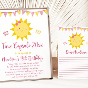May include: A pink and yellow time capsule card with a smiling sun illustration and butterflies. The card says "Time Capsule 20xx to be opened on Madison's 18th Birthday". The text below reads "Today I'll be one, time passes so fast! So let's make a special gift that will last. Write a sweet message, any will do. A memory, a prediction, we'll leave it up to you. Then when I grow up, a gift it will be to know just how much you all loved me!"