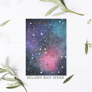 May include: A watercolor galaxy design with a dark blue, purple, and pink background with white and gold glitter accents. The text "INCLUDES BACK DESIGN" is printed at the bottom of the card.