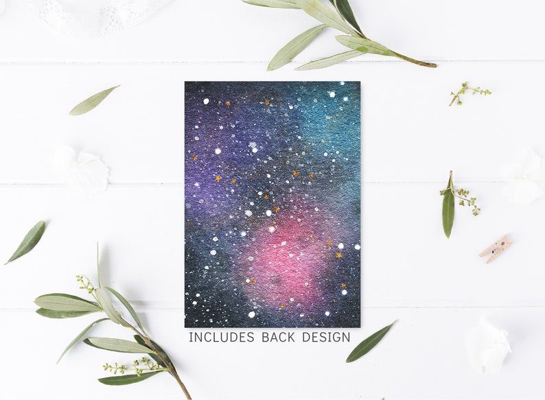 May include: A watercolor galaxy design with a dark blue, purple, and pink background with white and gold glitter accents. The text "INCLUDES BACK DESIGN" is printed at the bottom of the card.