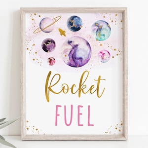 May include: A printable sign with a pink background and gold glitter. The sign features a watercolor illustration of planets and a rocket ship. The text "Rocket Fuel" is written in gold and pink lettering.