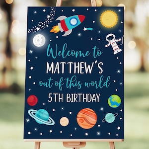 May include: A blue and white welcome sign with a rocket, planets, stars, and an astronaut. The sign says "Welcome to Matthew's Out of this World 5th Birthday".