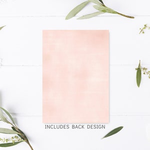 May include: A blank, light pink card with a subtle watercolor texture. The card is surrounded by sprigs of greenery and white flowers on a white wooden background. The text "INCLUDES BACK DESIGN" is printed below the card.