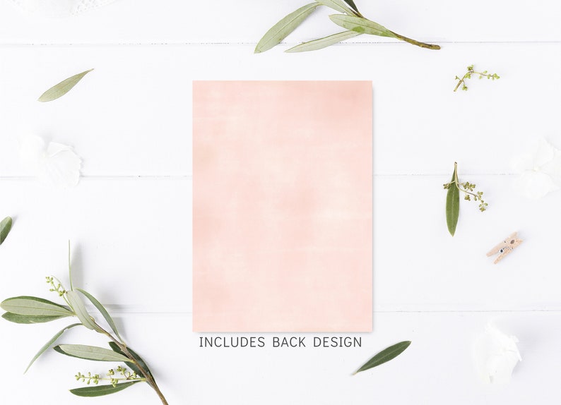 May include: A blank, light pink card with a subtle watercolor texture. The card is surrounded by sprigs of greenery and white flowers on a white wooden background. The text "INCLUDES BACK DESIGN" is printed below the card.