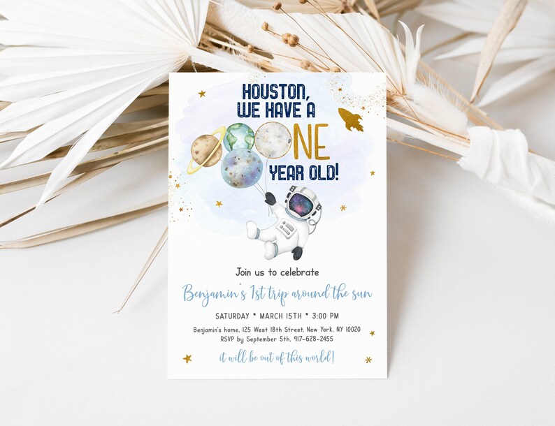 May include: A blue and gold astronaut-themed first birthday party invitation with a cartoon astronaut holding planets and a rocket ship. The text reads "Houston, we have a one year old!" and includes details for the party, including the date, time, and location.