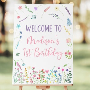 Puede incluir: Un cartel de bienvenida blanco con un borde floral. El cartel dice "Bienvenido a Madison's 1st Birthday" en letras rosa y morado.